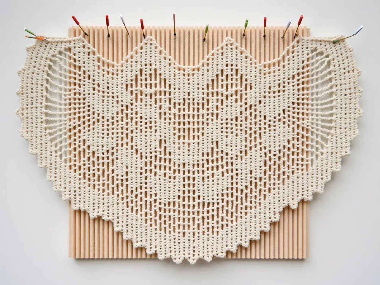 A crocheted lace shawl pinned out flat on a foam blocking mat with rustproof pins, showing the opened lace pattern